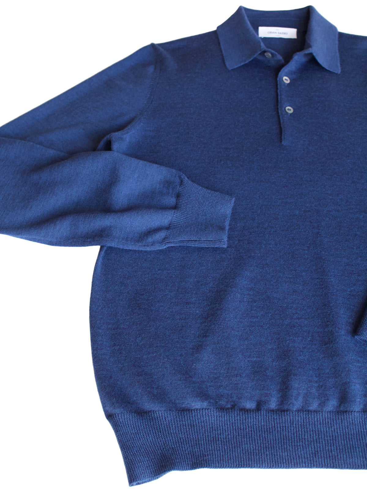 A long-sleeve knit polo sweater in a rich medium-to-dark blue, laid flat on a white surface with a hint of brown background at the top left.