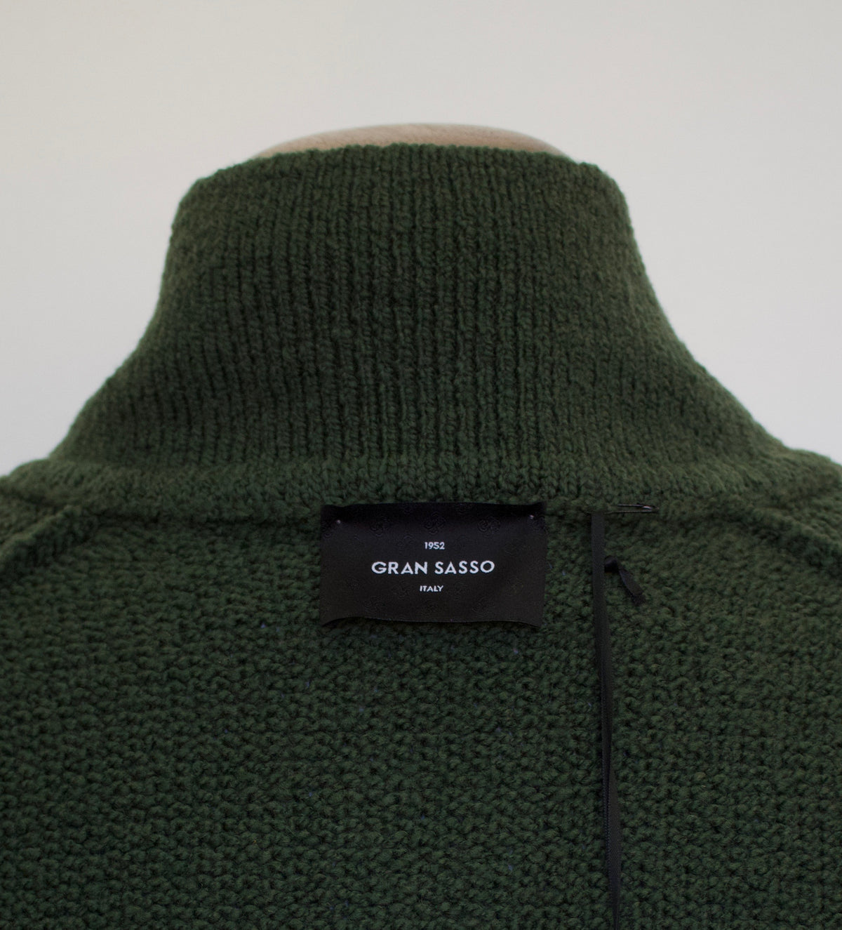 Close-up of the back of a dark olive green knit sweater on a mannequin, showing a black woven label that reads 'GRAN SASSO italy'.