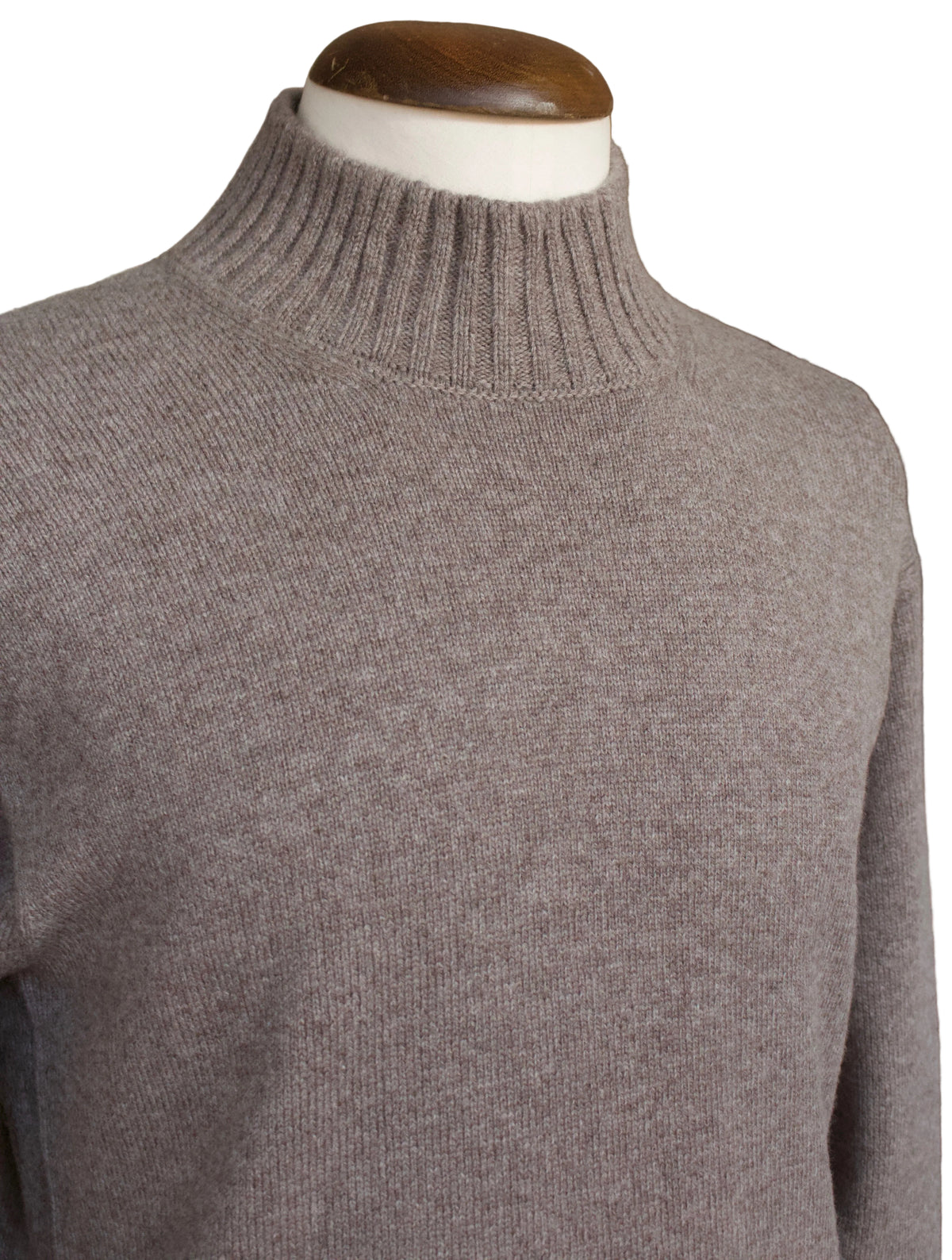 A close-up of a ribbed knit turtleneck sweater in a heathered taupe-gray color, displayed on a mannequin torso with a white neck and wooden head.