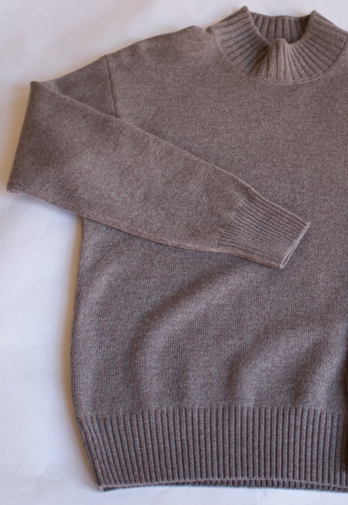 A taupe brown knit sweater with a mock neck, laid flat on a white background.