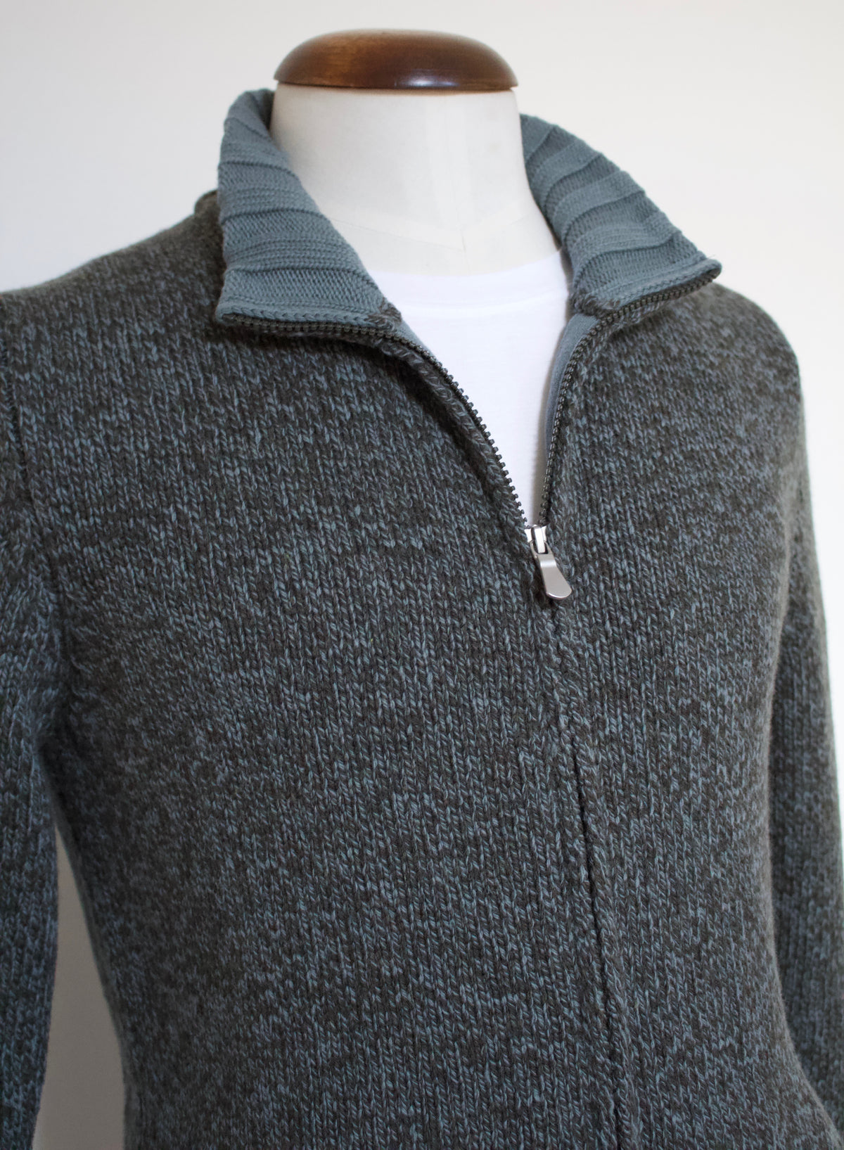 A green and brown heathered knit zip-up sweater with a ribbed mock neck collar, displayed on a white mannequin torso with a white undershirt.