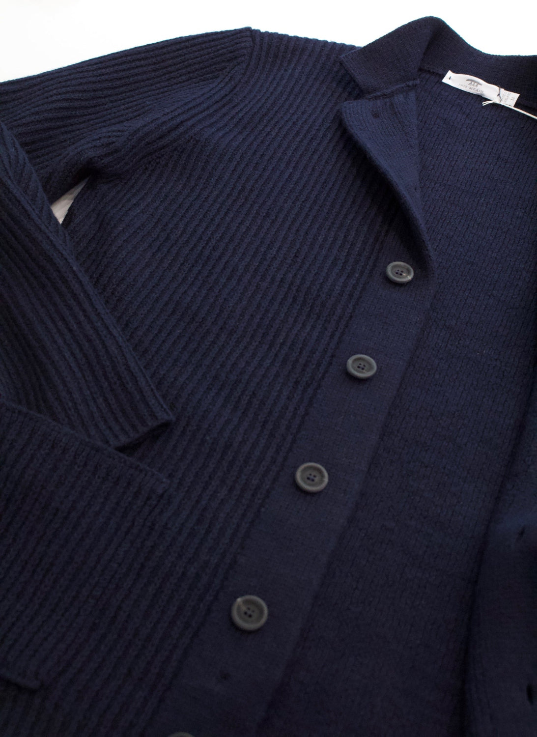 A close-up of a dark navy blue ribbed knit cardigan sweater with dark buttons, showing the collar and texture detail.