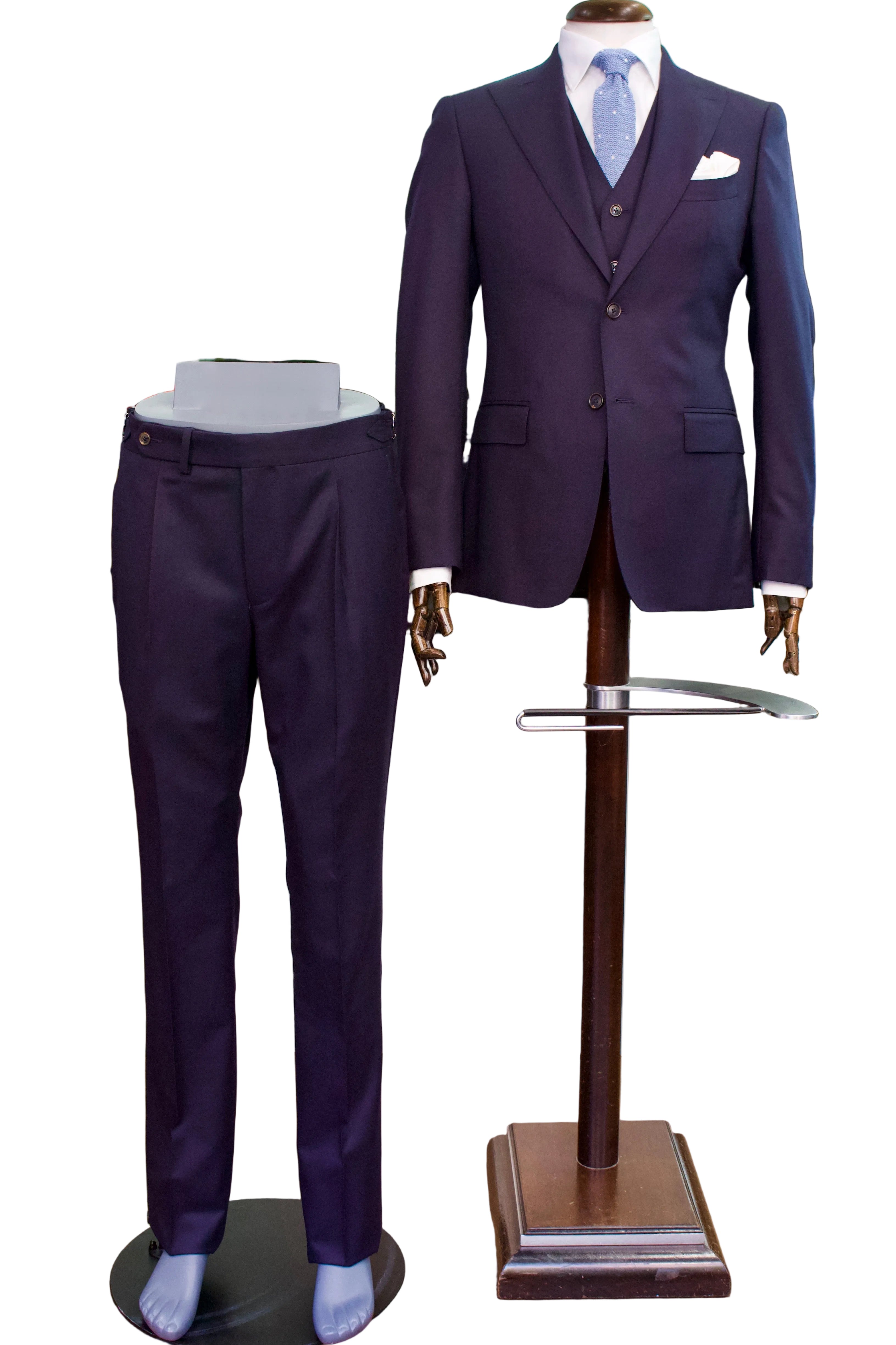 A men's formal suit displayed on mannequins in a clothing store. The set includes a dark purple three-piece suit with a matching vest and trousers, paired with a light blue patterned tie and white pocket square.
