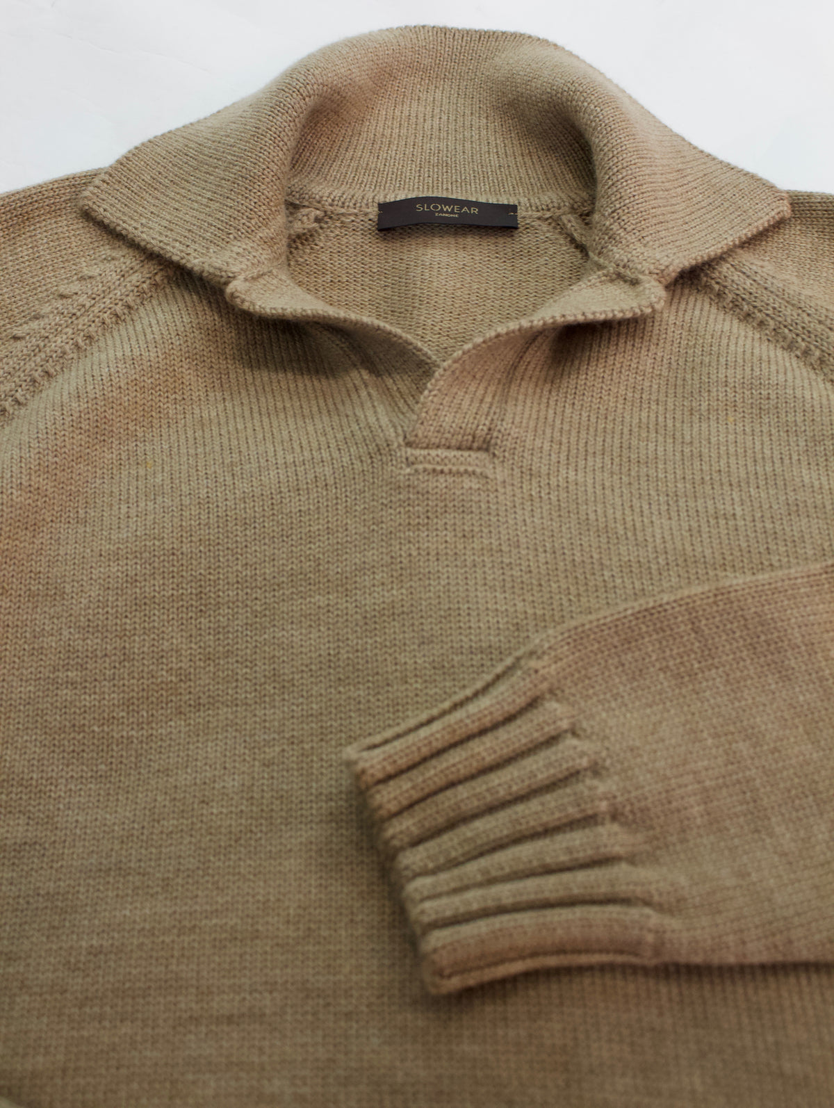 A close-up of a ribbed knit polo sweater in a warm taupe-brown color, showing the collar, sleeve cuff, and a small brown Slowear neck label.